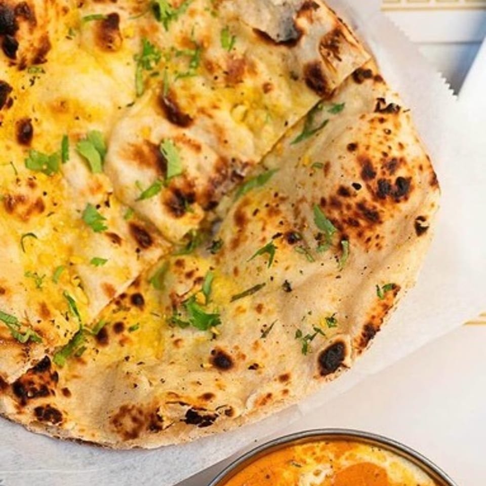 Grilled naan topped with herbs beside a bowl of creamy orange curry on a patterned plate.