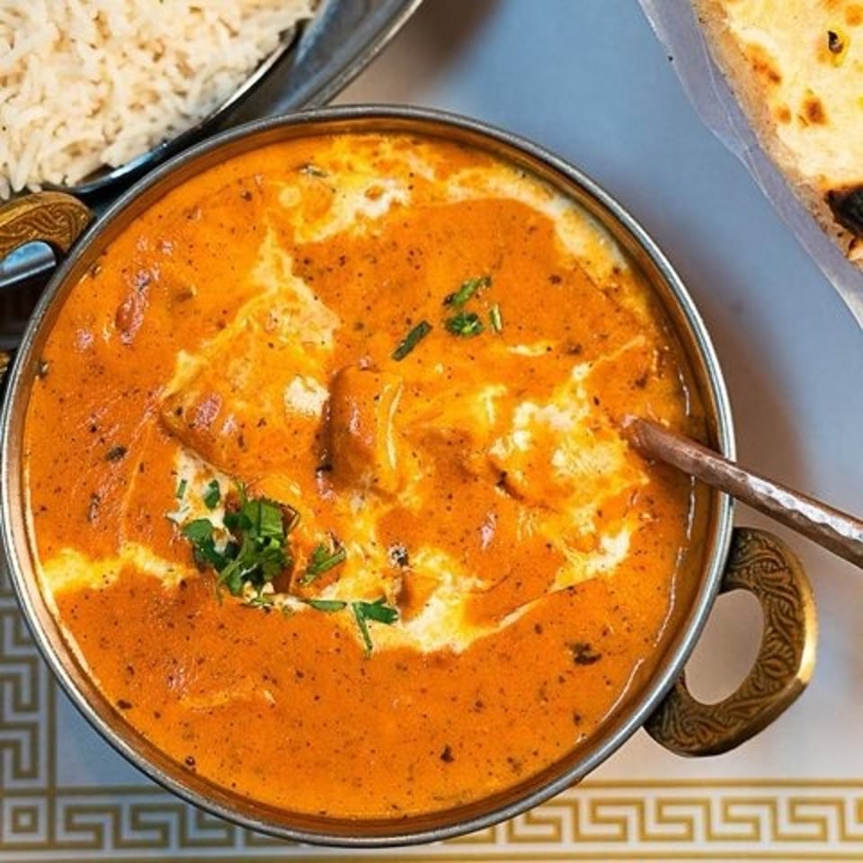 Creamy orange curry garnished with cilantro, served in a metal bowl alongside rice and naan on a patterned plate.