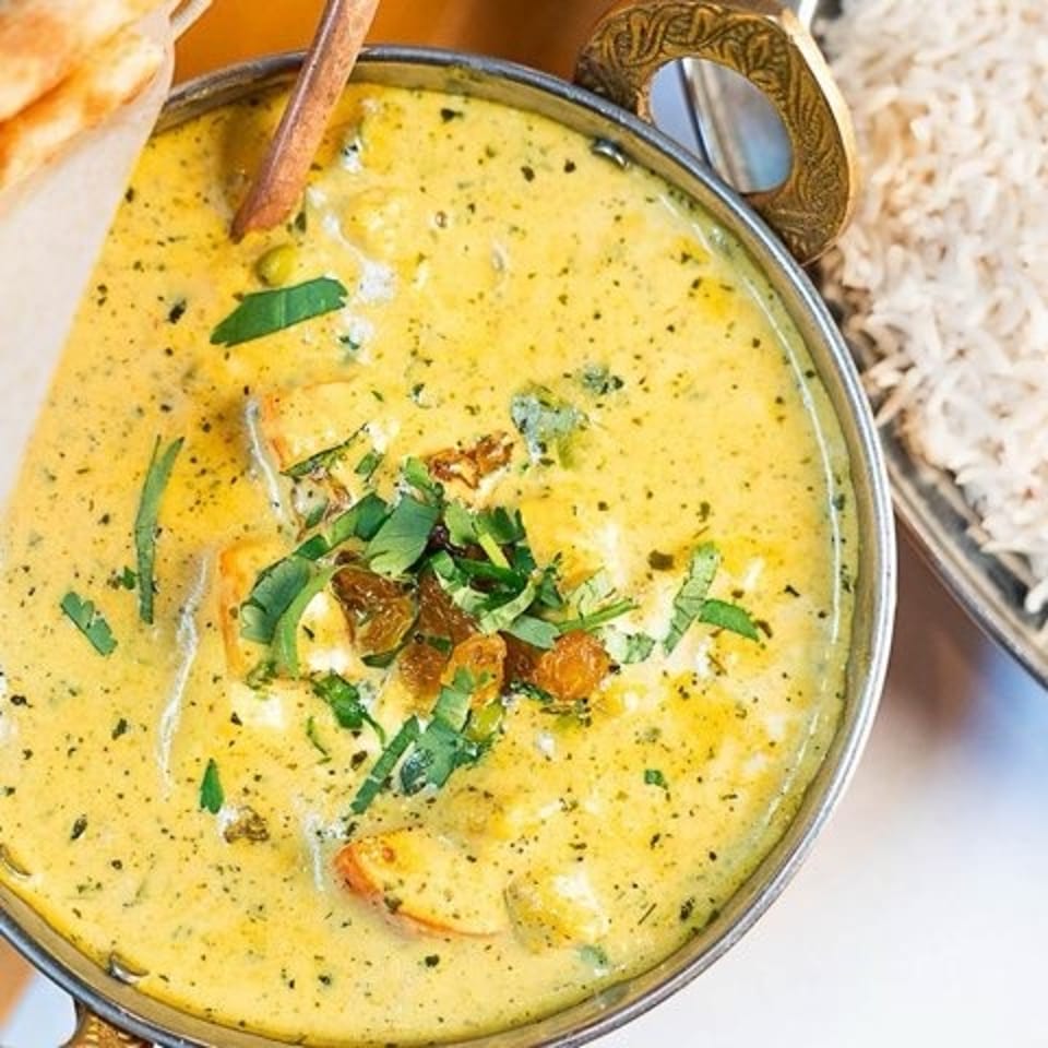 Creamy yellow curry garnished with herbs and vegetables, served with rice and naan.
